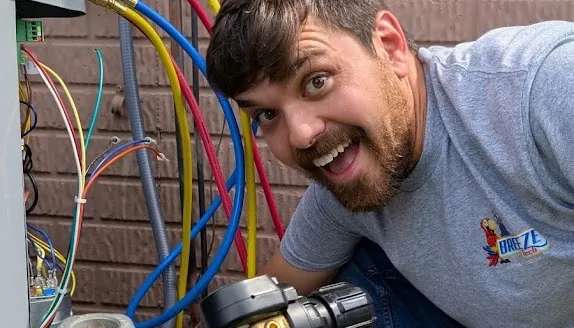 BreezeTech Heating and Cooling technician grinning while pressure testing refrigerant lines with manifold gauges