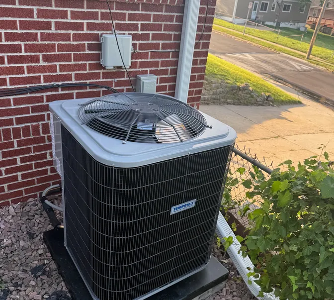 Air conditioner condenser beside a brick home, serviced by BreezeTech Heating and Cooling