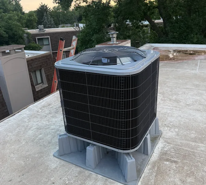 New air conditioner condenser mounted on a rooftop stand by BreezeTech Heating and Cooling