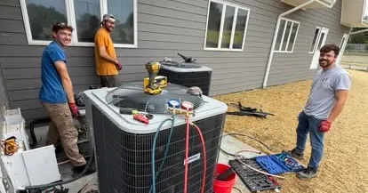 Three BreezeTech technicians installing a new air conditioner beside a home