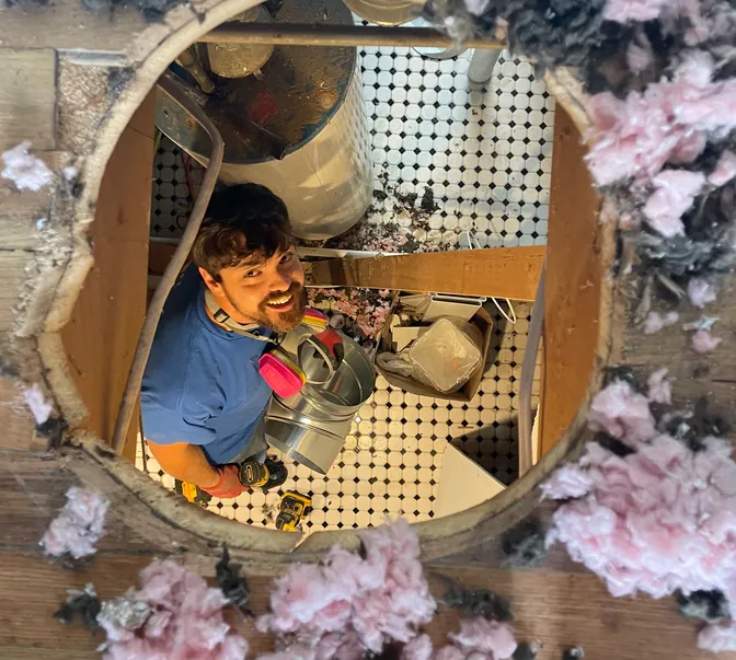 BreezeTech Heating and Cooling technician seen through a ceiling opening while running new ductwork