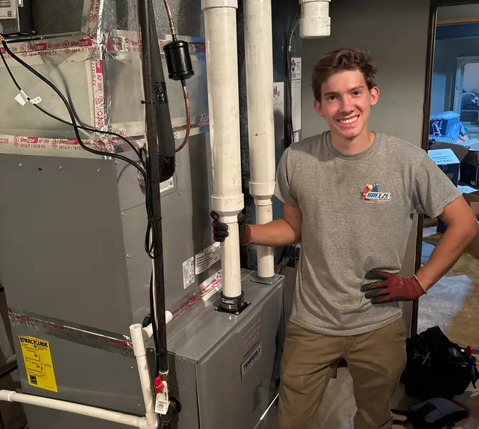 Smiling BreezeTech Heating and Cooling technician standing next to a newly installed high-efficiency furnace