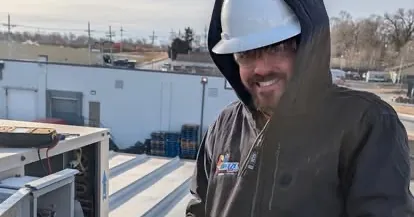 A BreezeTech technician in a hard hat on a commercial rooftop beside a rooftop unit