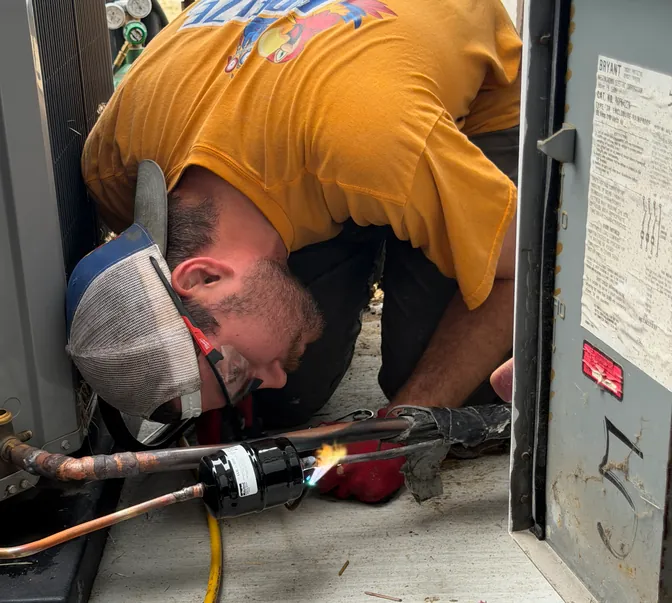 BreezeTech Heating and Cooling technician brazing refrigerant lines at a condenser