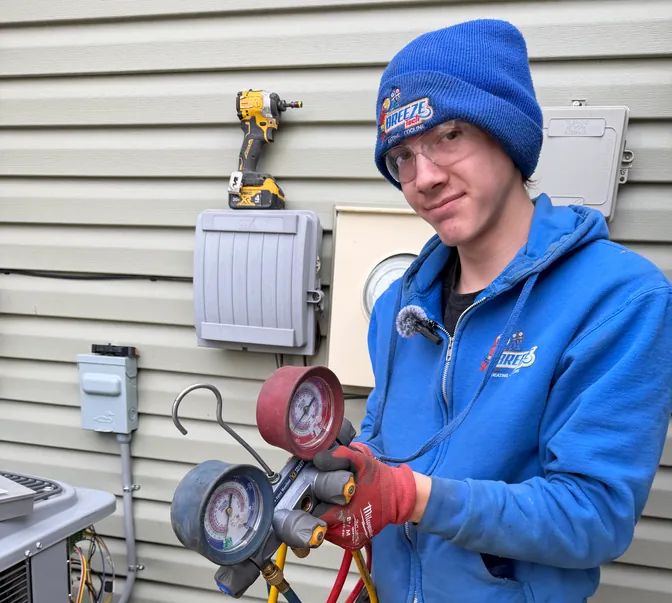 BreezeTech Heating and Cooling technician holding refrigerant manifold gauges next to a condenser