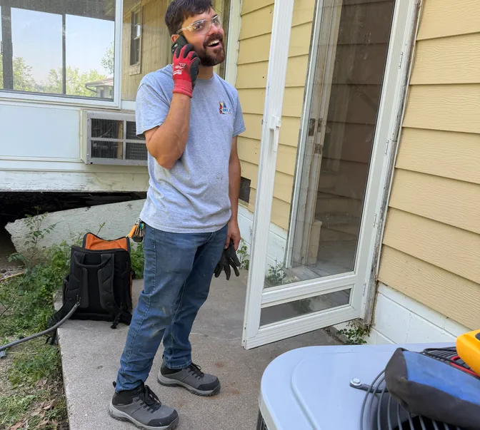 BreezeTech Heating and Cooling technician on a phone call beside a customer's air conditioner