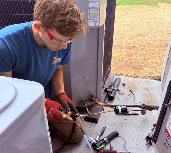 BreezeTech Heating and Cooling technician brazing refrigerant fittings at a commercial condensing unit