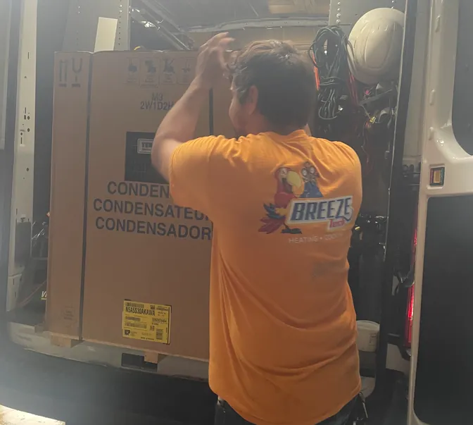 BreezeTech Heating and Cooling technician loading a new condenser into a service van