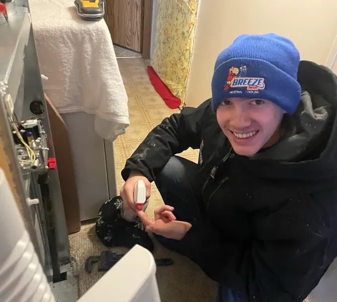 Smiling BreezeTech Heating and Cooling technician servicing a furnace