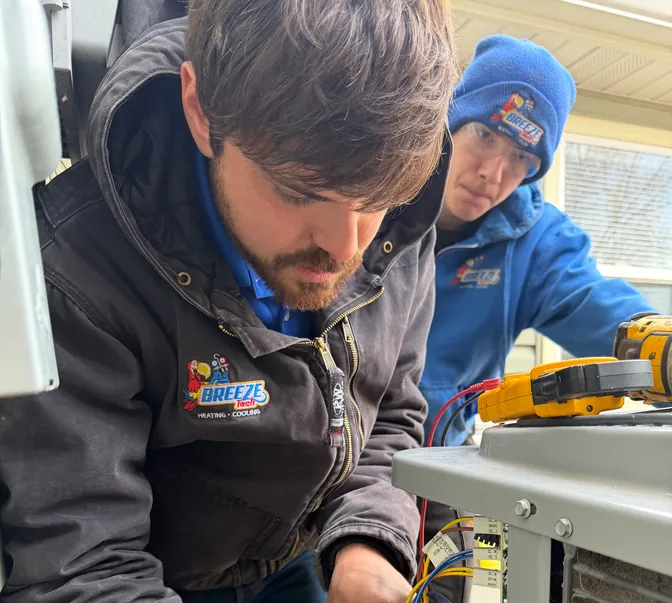 Two BreezeTech Heating and Cooling technicians troubleshooting air conditioner wiring