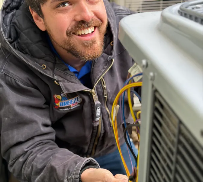 Smiling BreezeTech Heating and Cooling technician wiring an air conditioner condenser