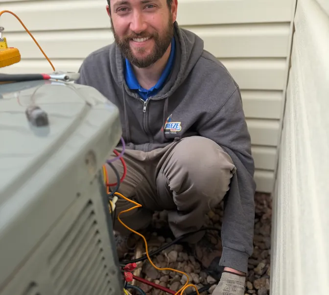 Smiling BreezeTech Heating and Cooling technician servicing an outdoor AC unit