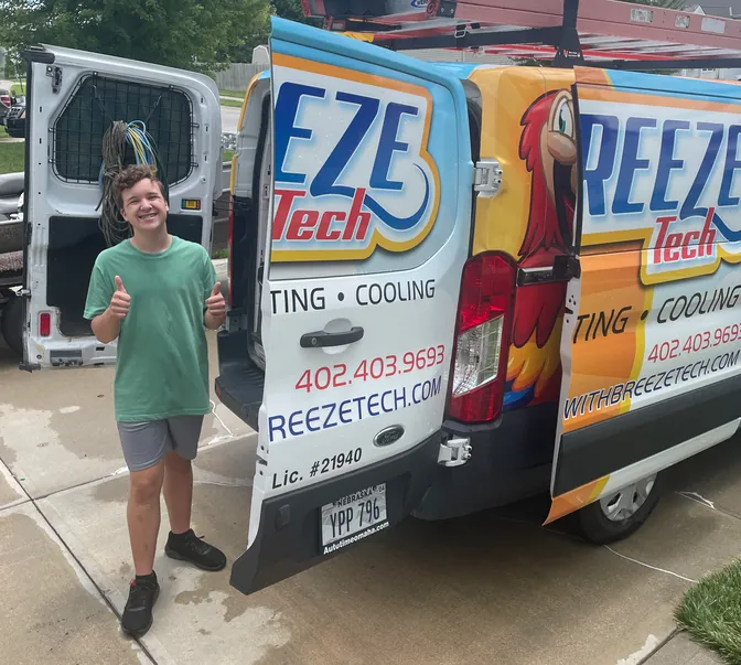 Young helper giving a thumbs up beside a BreezeTech Heating and Cooling service van