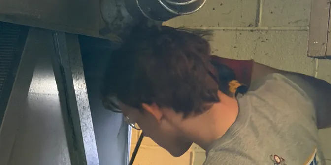BreezeTech Heating and Cooling technician working on a furnace cabinet in a basement