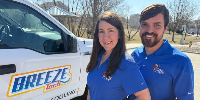 Kayla and Micah, the husband-and-wife team behind BreezeTech Heating and Cooling, in matching blue polos beside their work truck