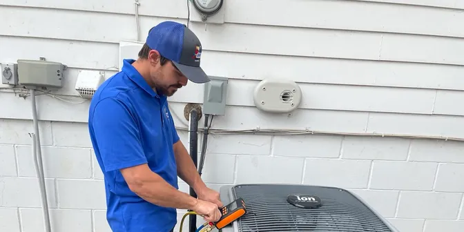 BreezeTech Heating and Cooling technician testing an air conditioner with a digital manifold gauge