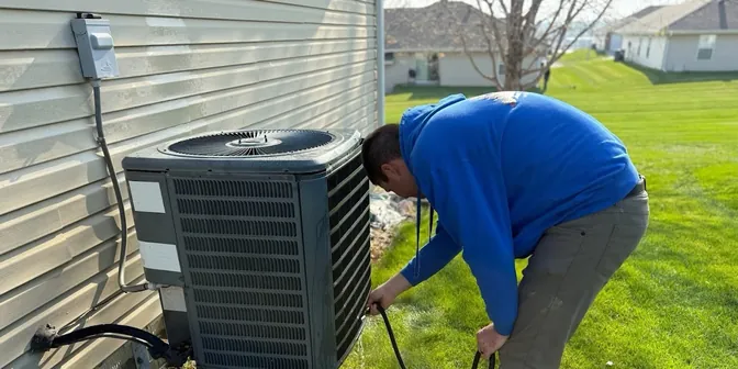 BreezeTech Heating and Cooling technician servicing a residential air conditioner in a backyard