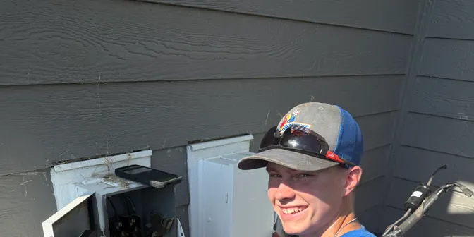 Smiling BreezeTech Heating and Cooling technician wiring an electrical disconnect for a new AC
