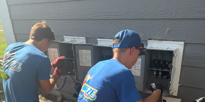 Two BreezeTech Heating and Cooling technicians wiring disconnects for new outdoor units