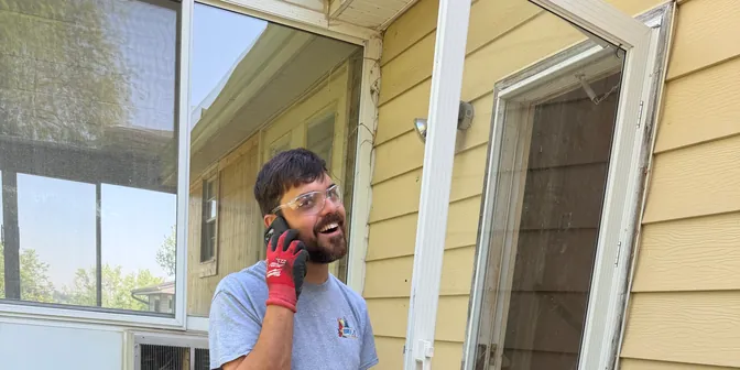 BreezeTech Heating and Cooling technician on a phone call beside a customer's air conditioner