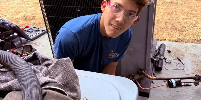 Smiling BreezeTech Heating and Cooling technician behind a condensing unit during an install
