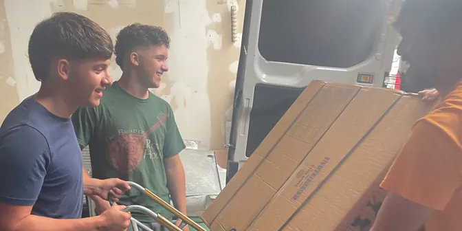 BreezeTech Heating and Cooling crew moving a boxed air conditioner with a hand truck