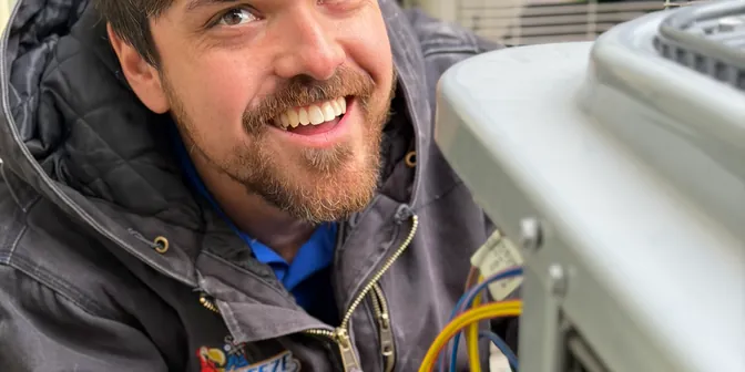 Smiling BreezeTech Heating and Cooling technician wiring an air conditioner condenser