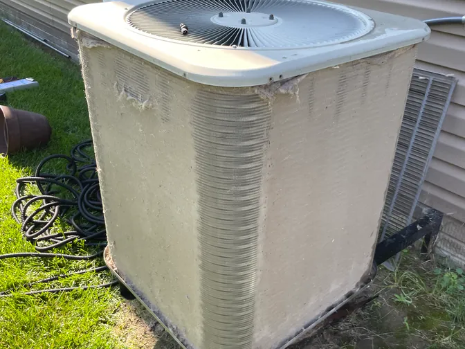 An air conditioner condenser with a dirt-clogged coil before cleaning