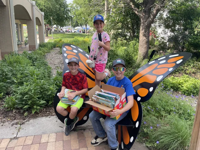 Kids with stacks of books on a butterfly bench at Sump Memorial Library