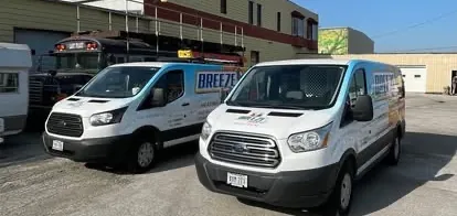 Two BreezeTech Heating and Cooling branded service vans parked outside the shop