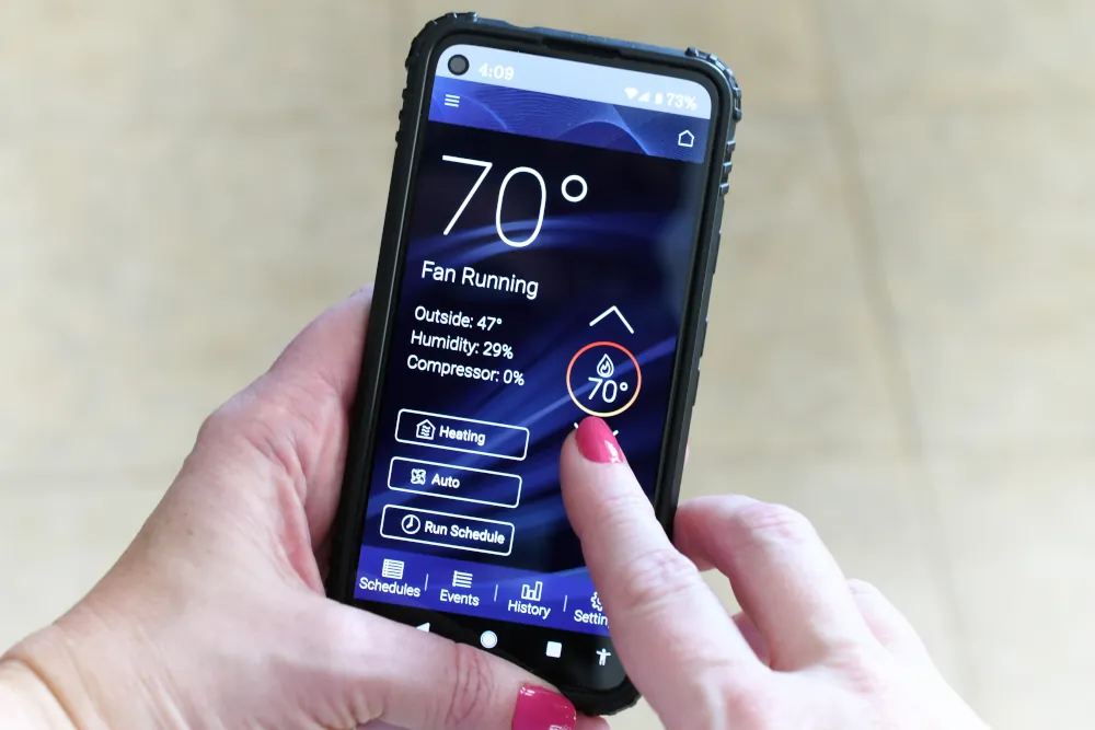 Female adjusting heating cooling thermostat via an app on her phone.